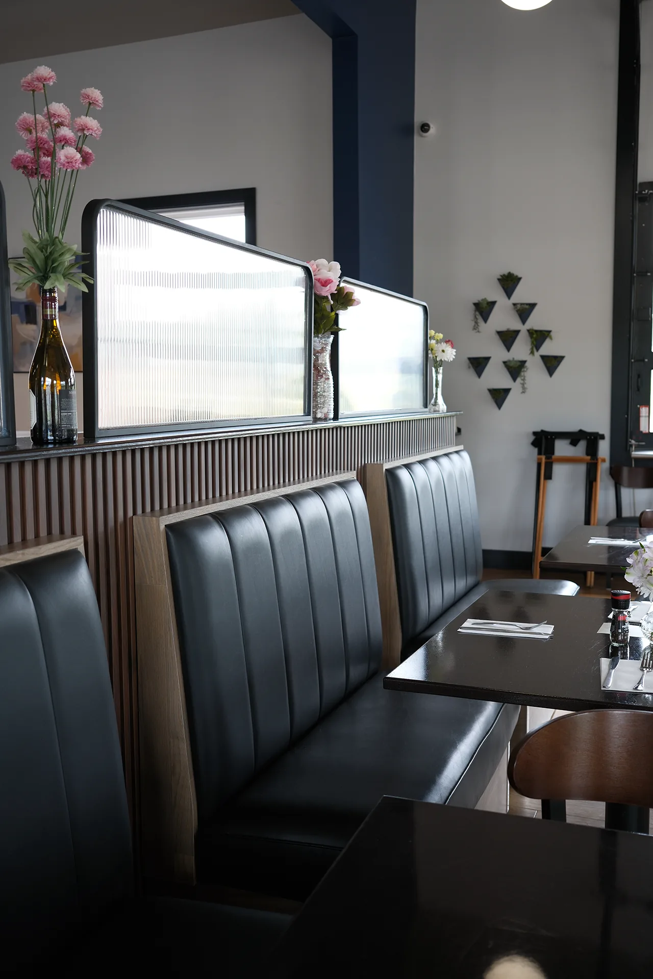 Black leather booths with ribbed glass dividers and vases of flowers along the top Black leather booths with ribbed glass dividers and vases of flowers along the top