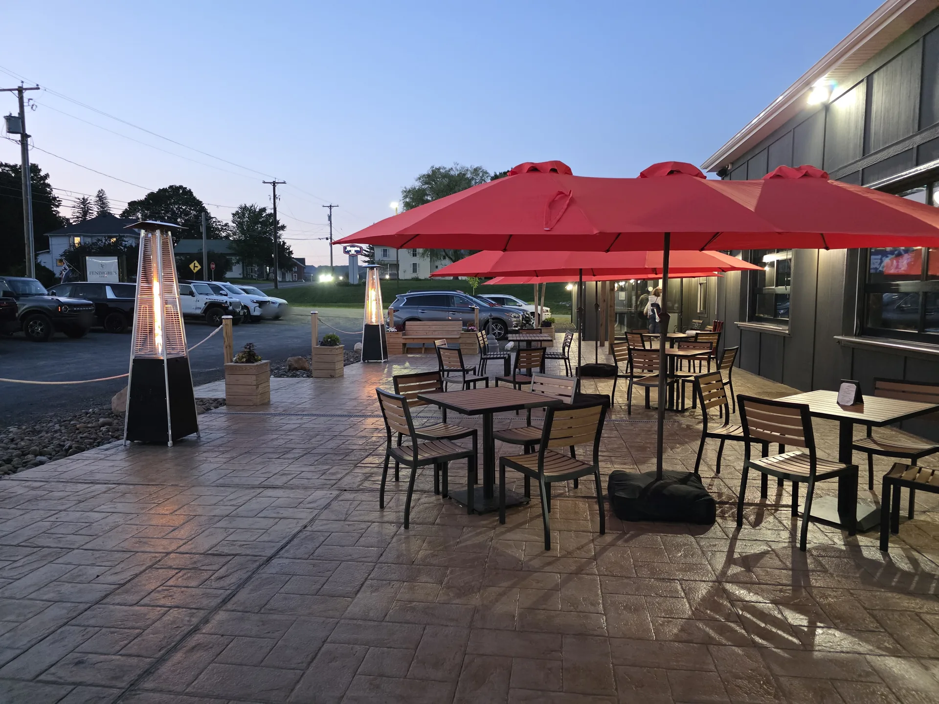 The Fenimore's Table patio at dusk, with red umbrellas over empty tables and lit patio heaters along the rope railing The Fenimore's Table patio at dusk, with red umbrellas over empty tables and lit patio heaters along the rope railing