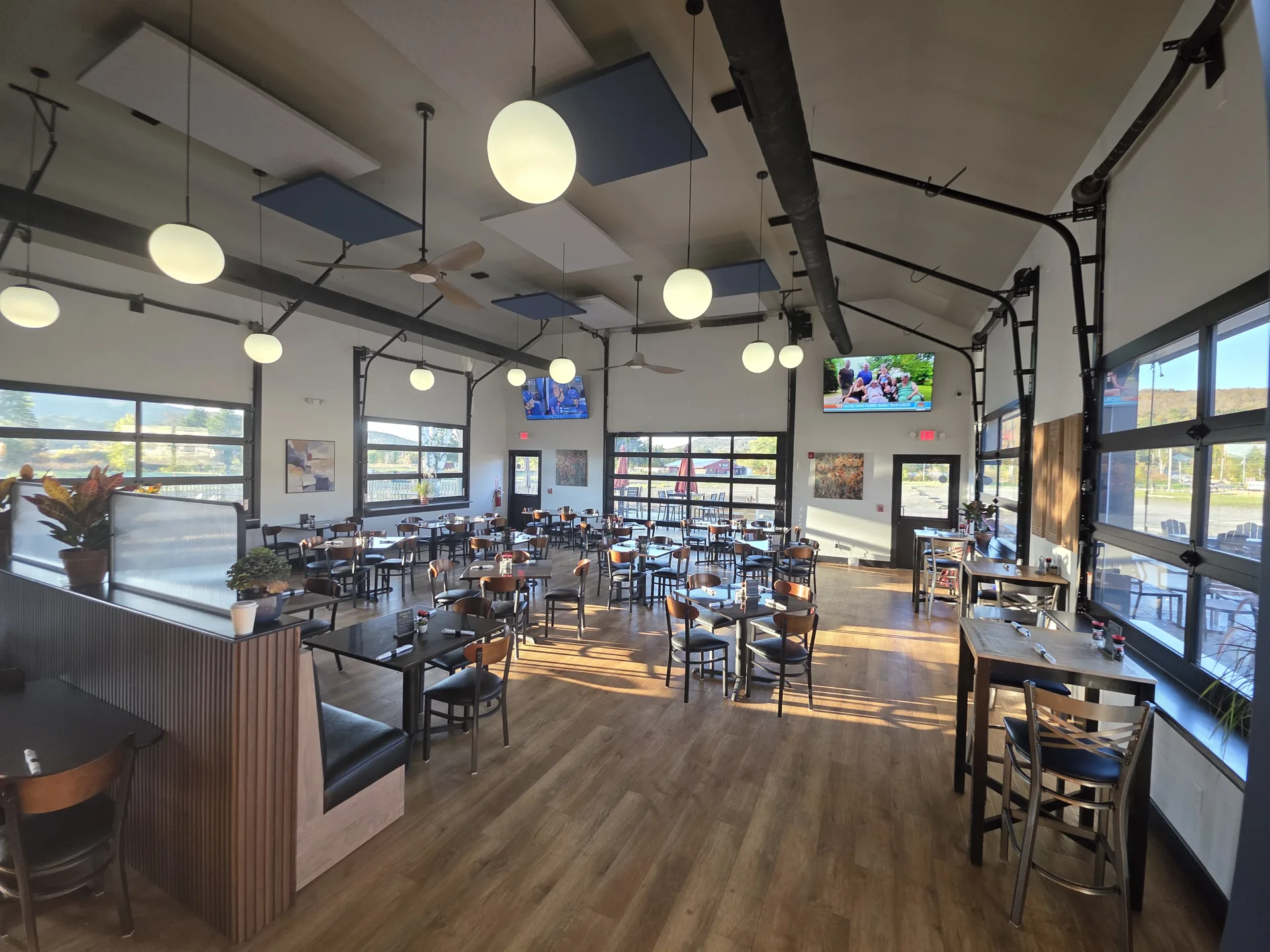 The event room at Fenimore's Table in daylight: white walls, black-framed glass garage doors, globe pendant lights and tables set along the windows The event room at Fenimore's Table in daylight: white walls, black-framed glass garage doors, globe pendant lights and tables set along the windows