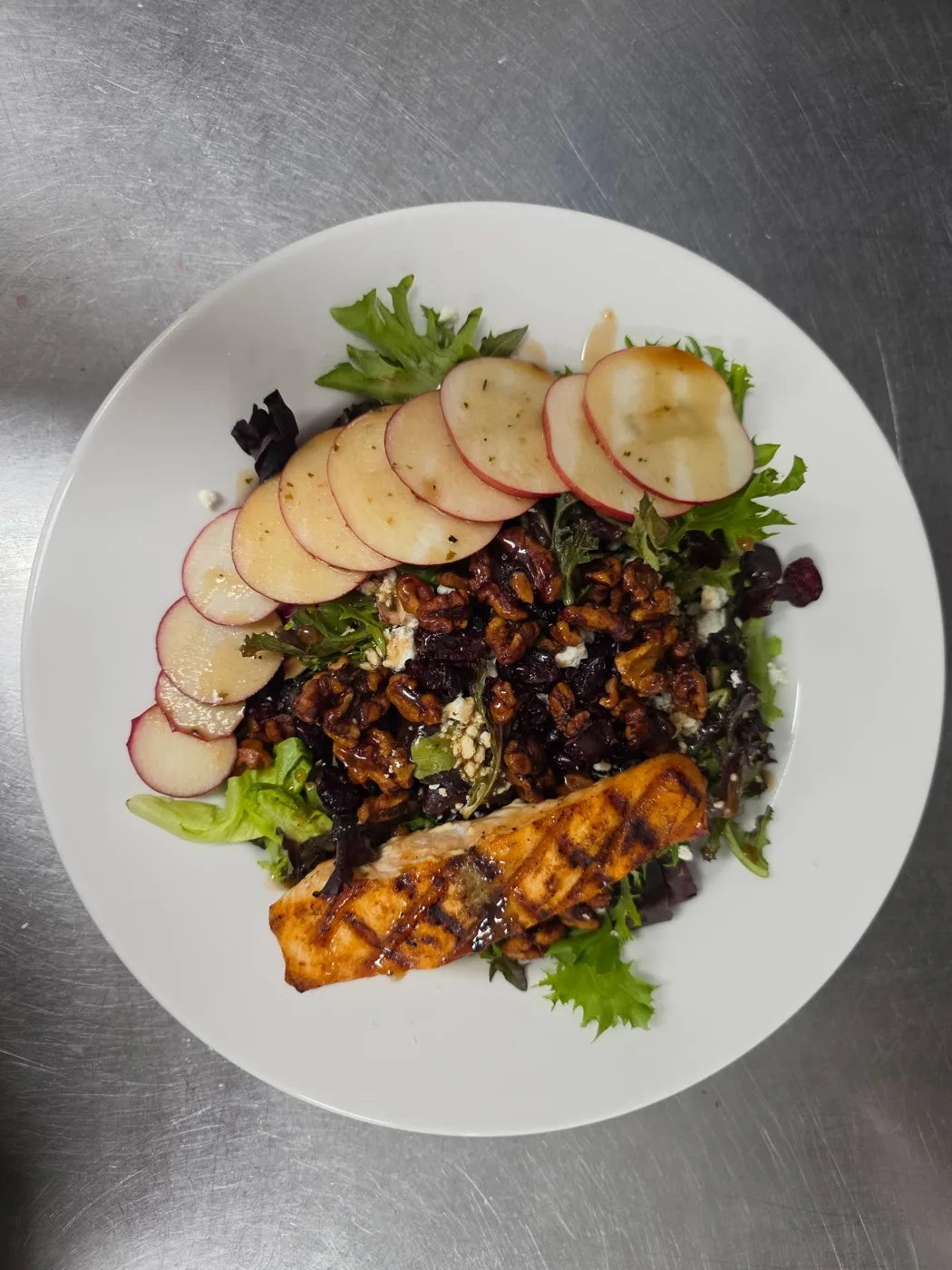 A plated salad of mixed greens, sliced apple, candied walnuts and grilled salmon A plated salad of mixed greens, sliced apple, candied walnuts and grilled salmon
