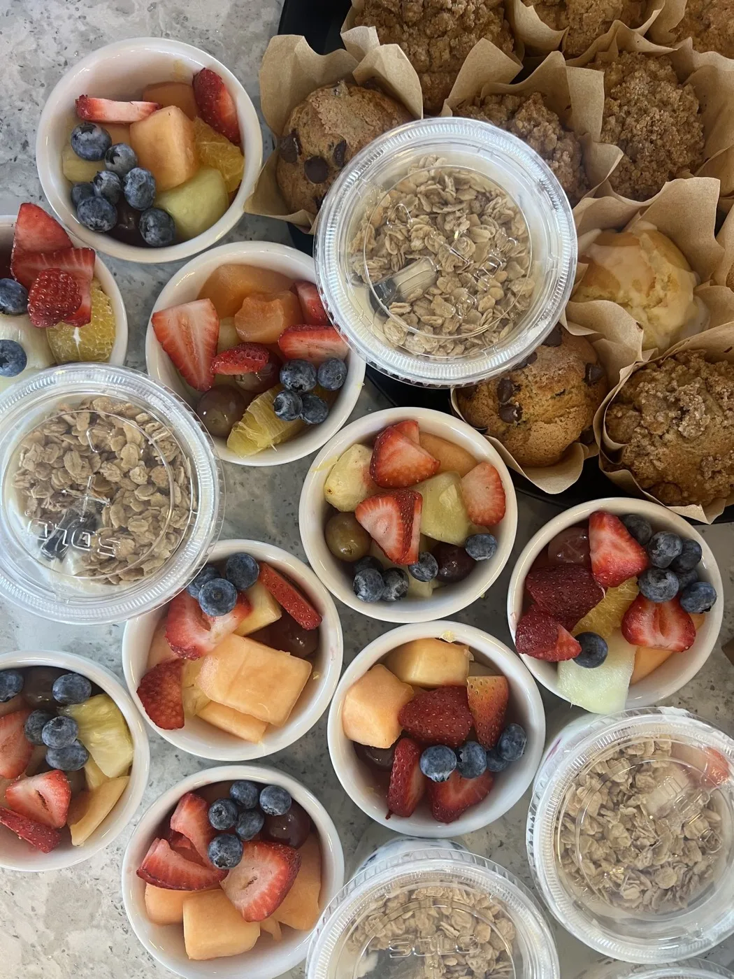 Cups of fresh cut fruit and granola beside muffins in paper wraps Cups of fresh cut fruit and granola beside muffins in paper wraps